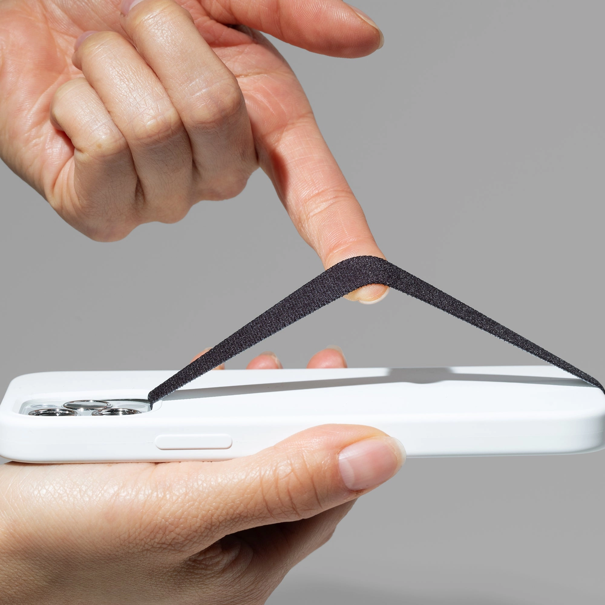 A fingertip stretching a black SteadyStraps strap over the back of a white phone