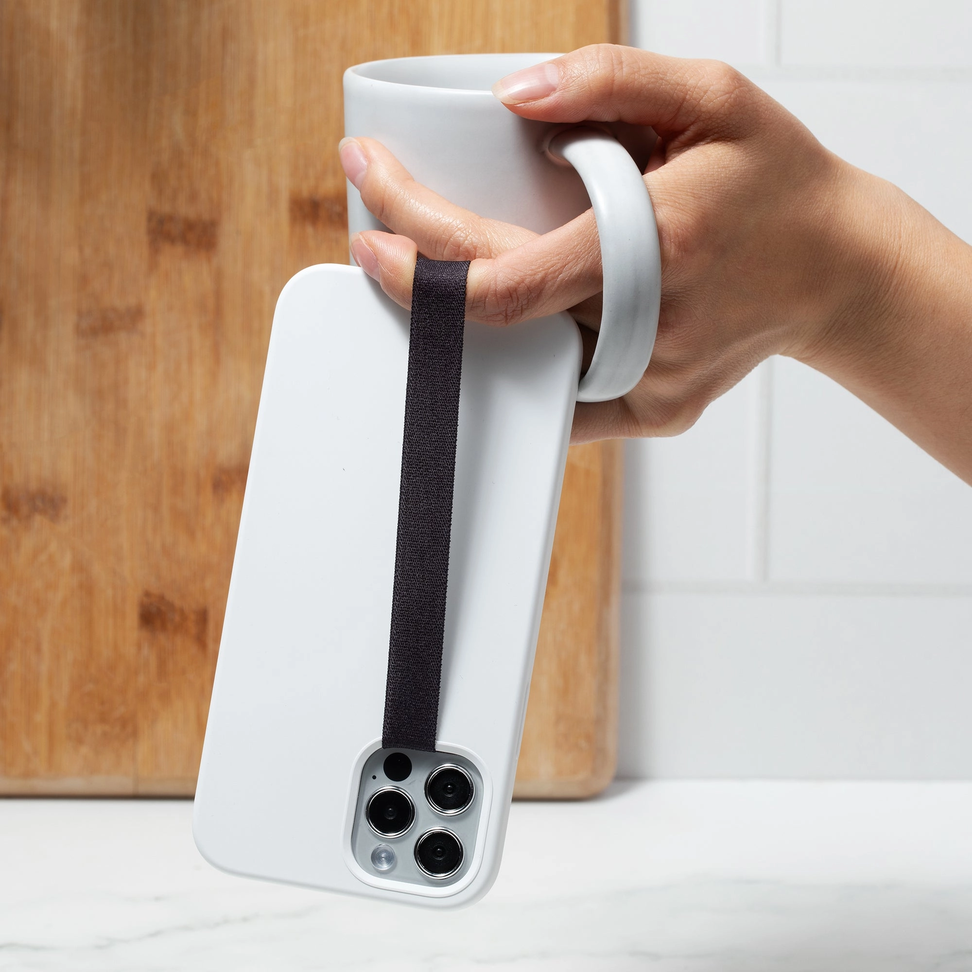 A hand holding a white mug by a black SteadyStraps strap on the back of a phone
