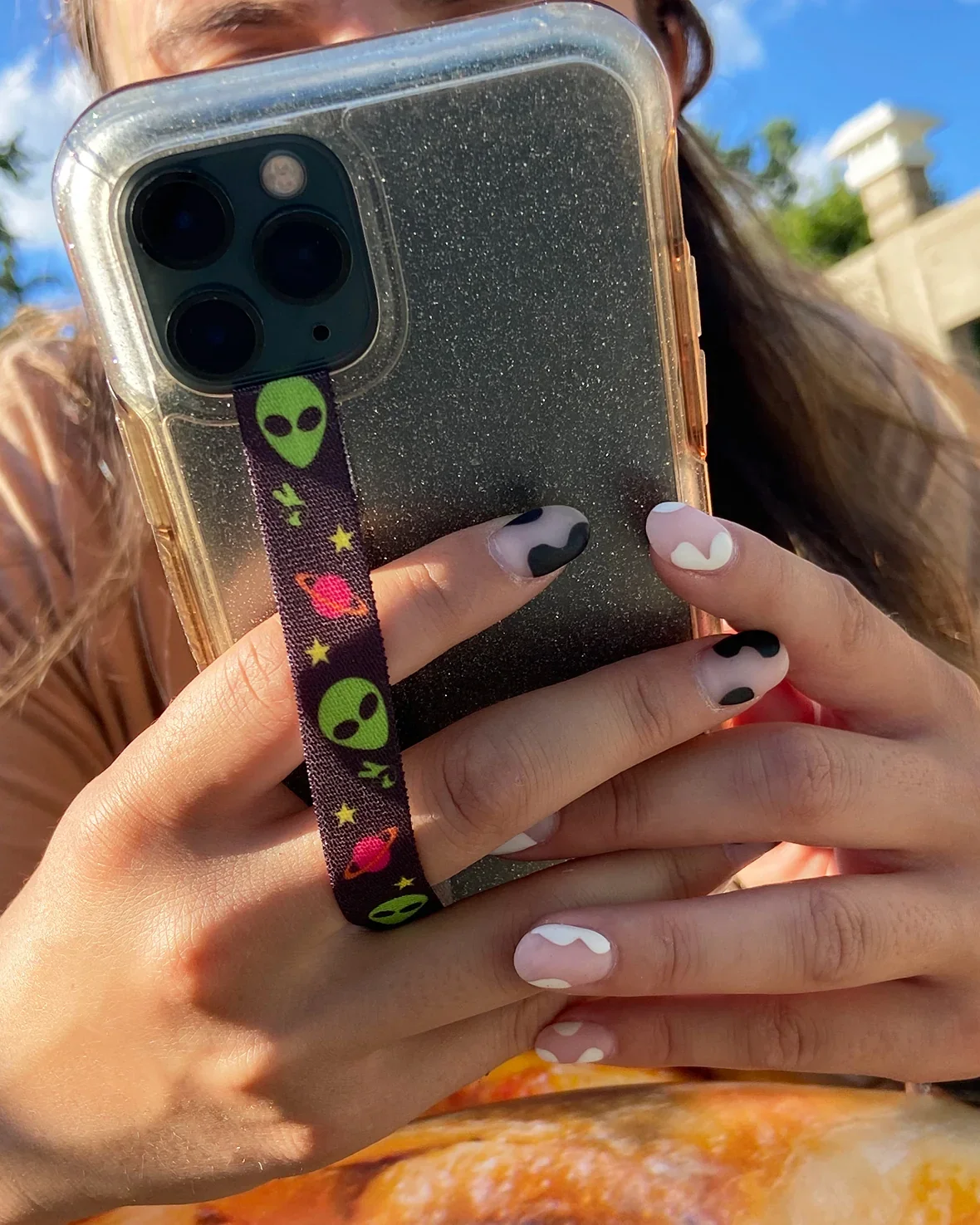 A person holding a phone with an alien-print strap