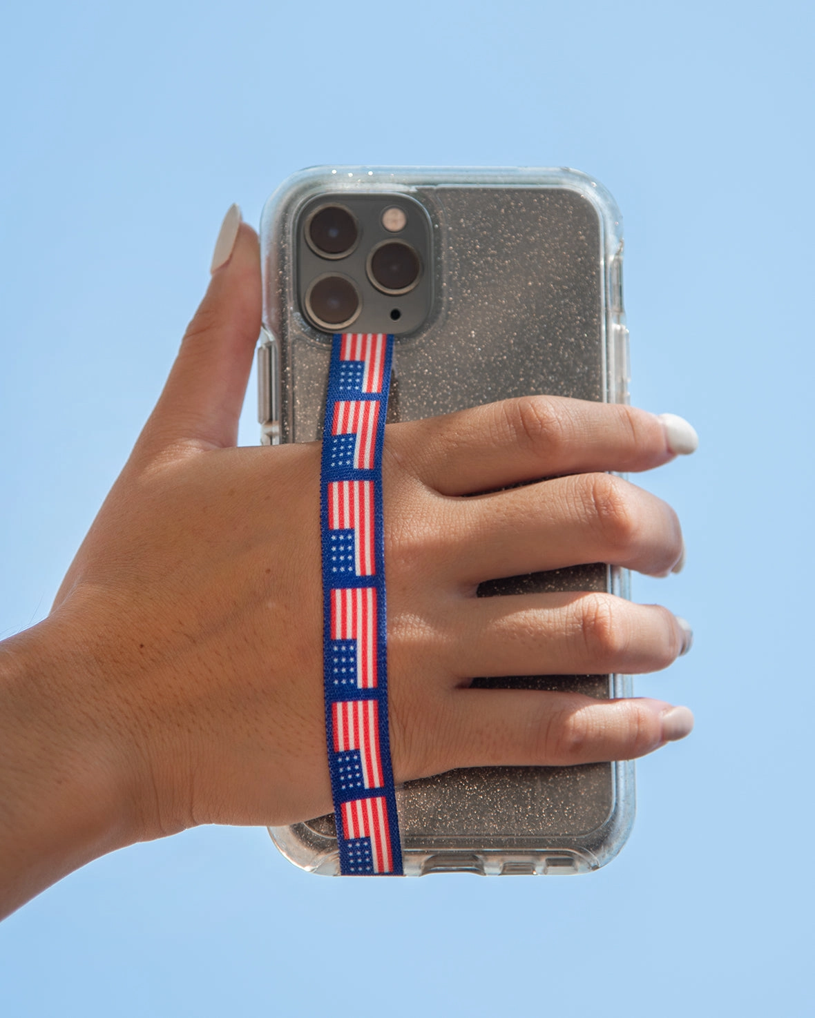 A hand holding a phone with a U.S. Flag strap against a blue sky